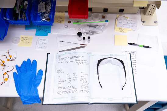 A notebook lays open with gloves and safety glasses.